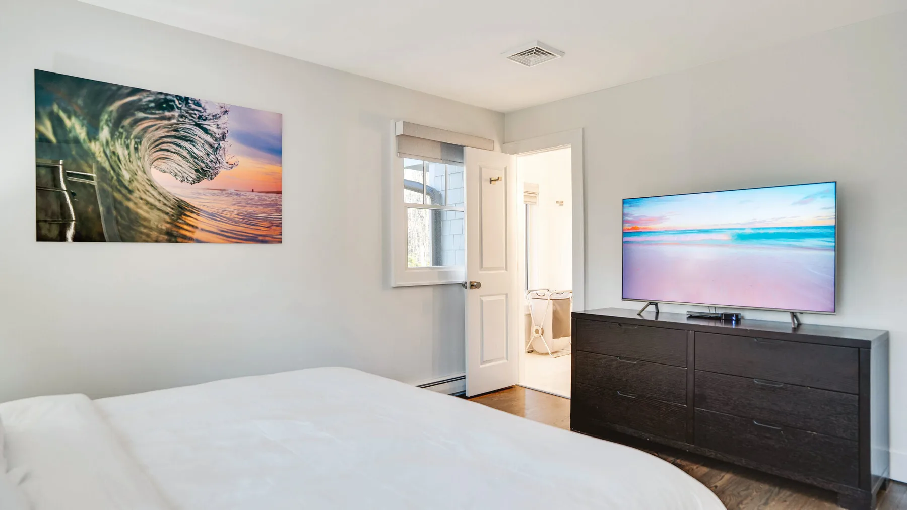 A bedroom with a bed, wall art, and a television on a dresser.
