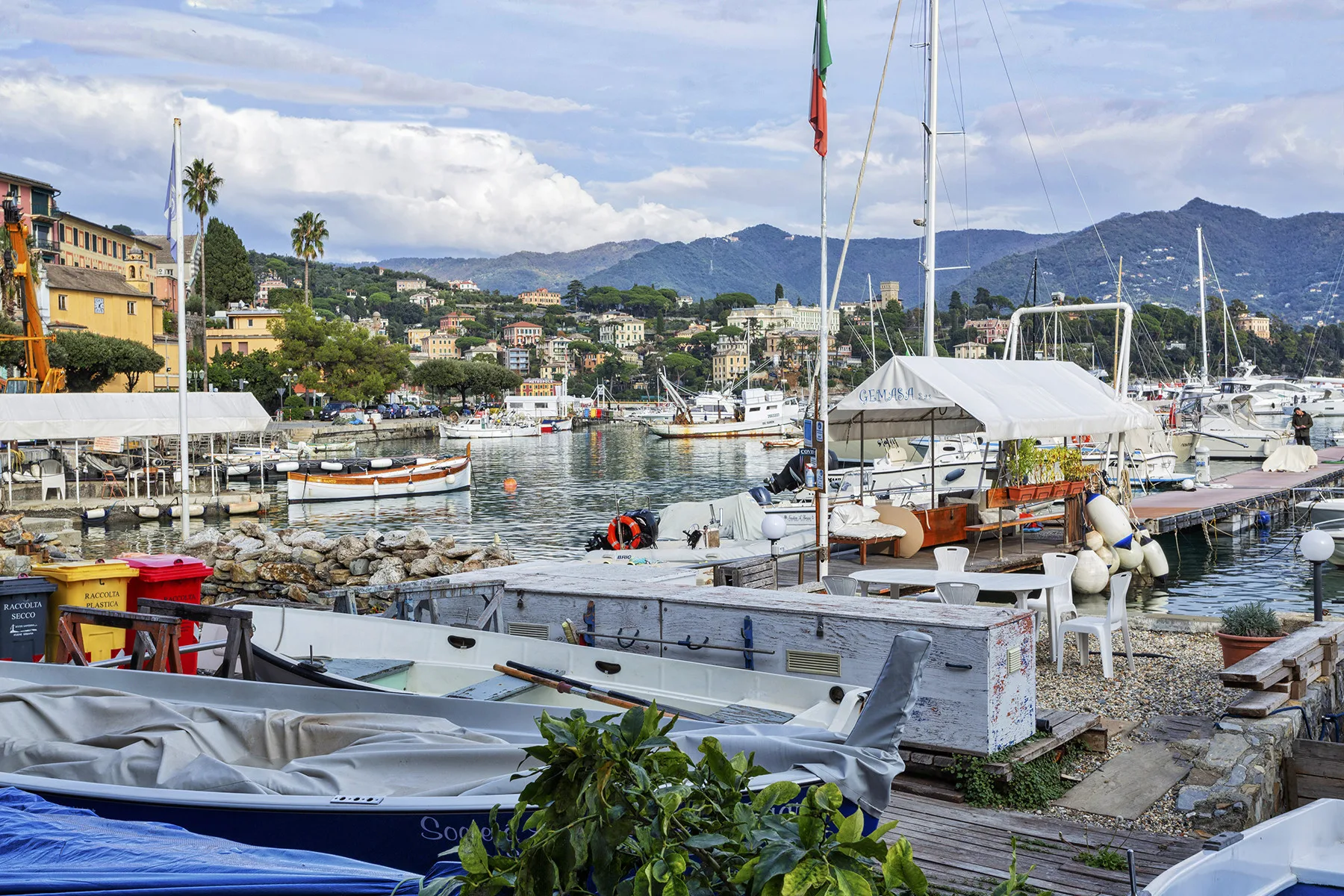 Un puerto deportivo con barcos en primer plano y un pueblo costero bajo las colinas.