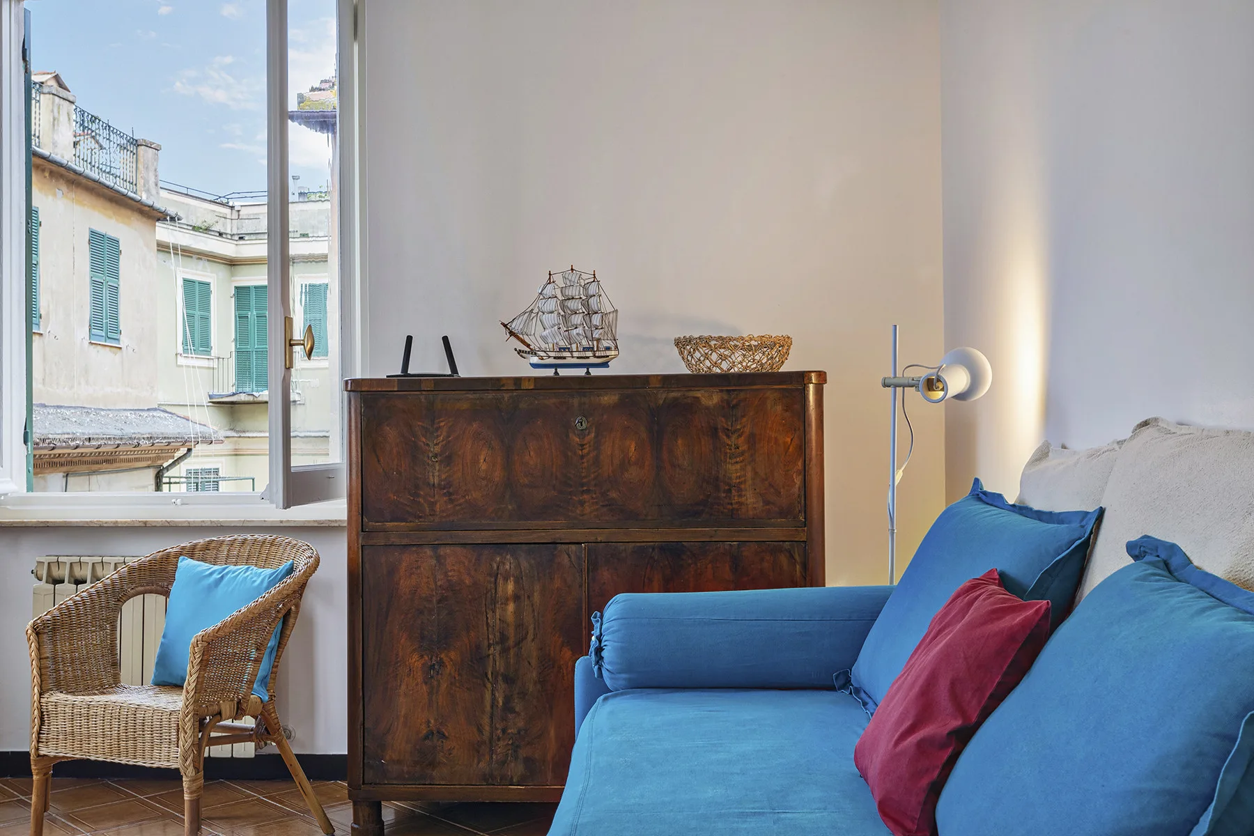Una sala de estar con asientos azules junto a un mueble oscuro y una ventana amplia.