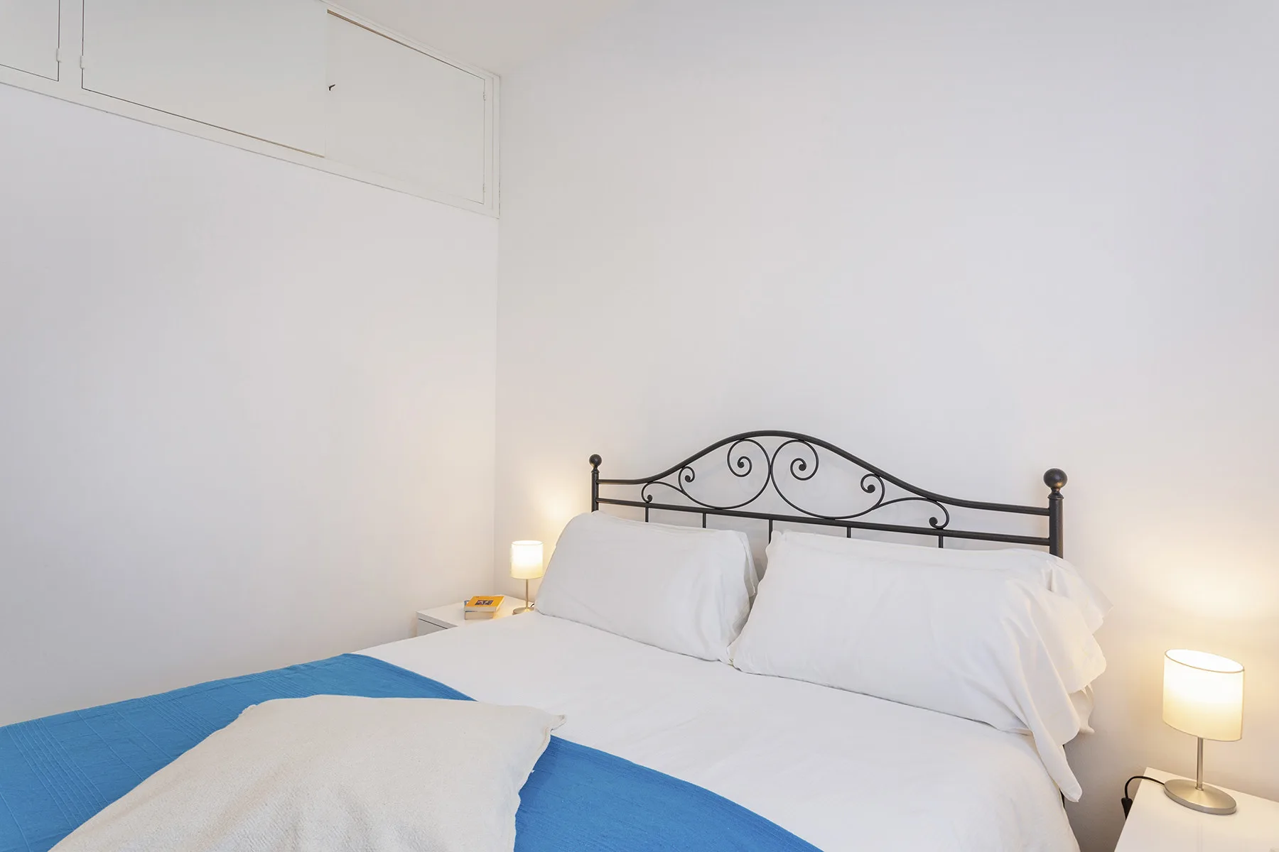 Un dormitorio con ropa de cama blanca, detalles azules y un cabecero metálico oscuro.
