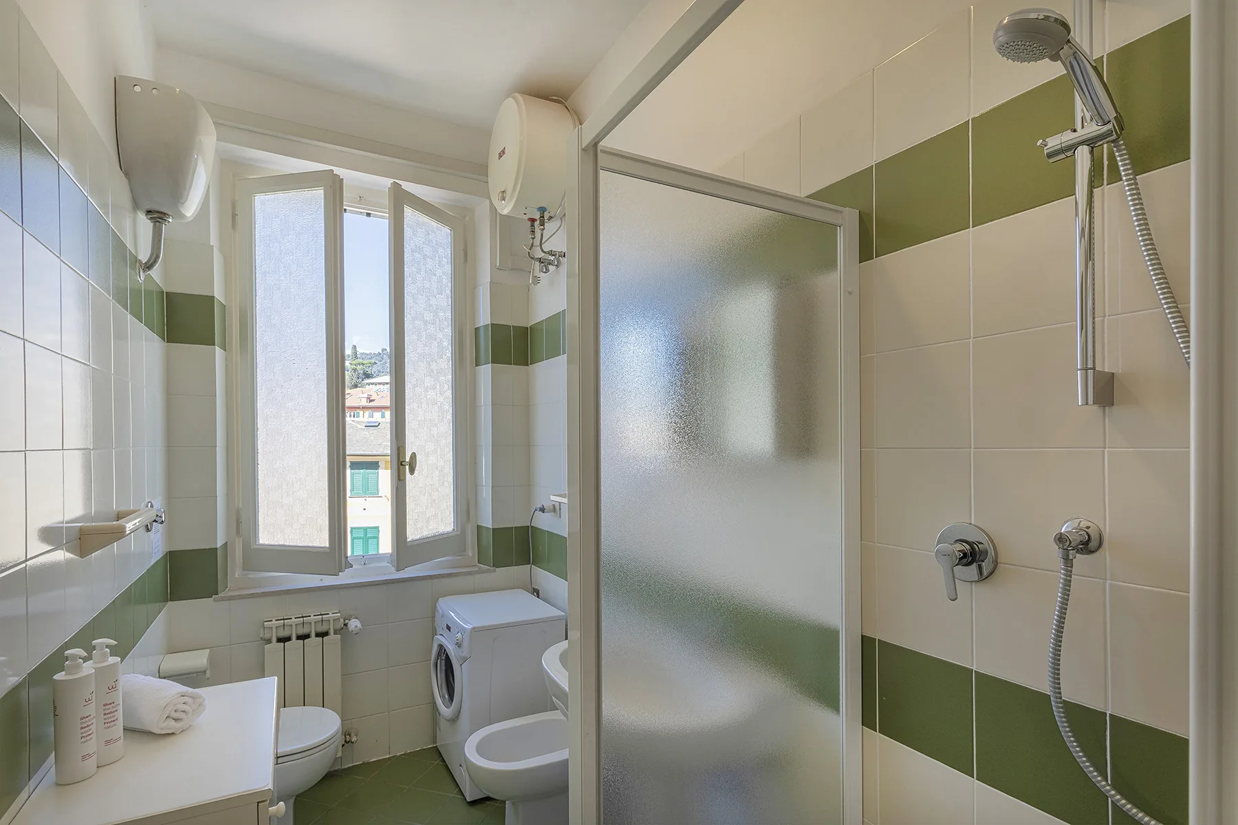 Un baño alicatado con ducha, inodoro, lavabo y una ventana.