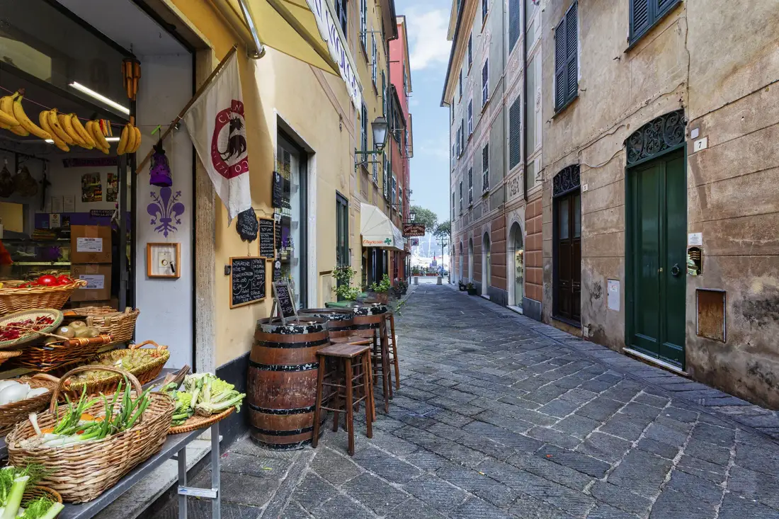 Una calle estrecha pavimentada con piedra pasa entre edificios antiguos, con un puesto de mercado a la izquierda.