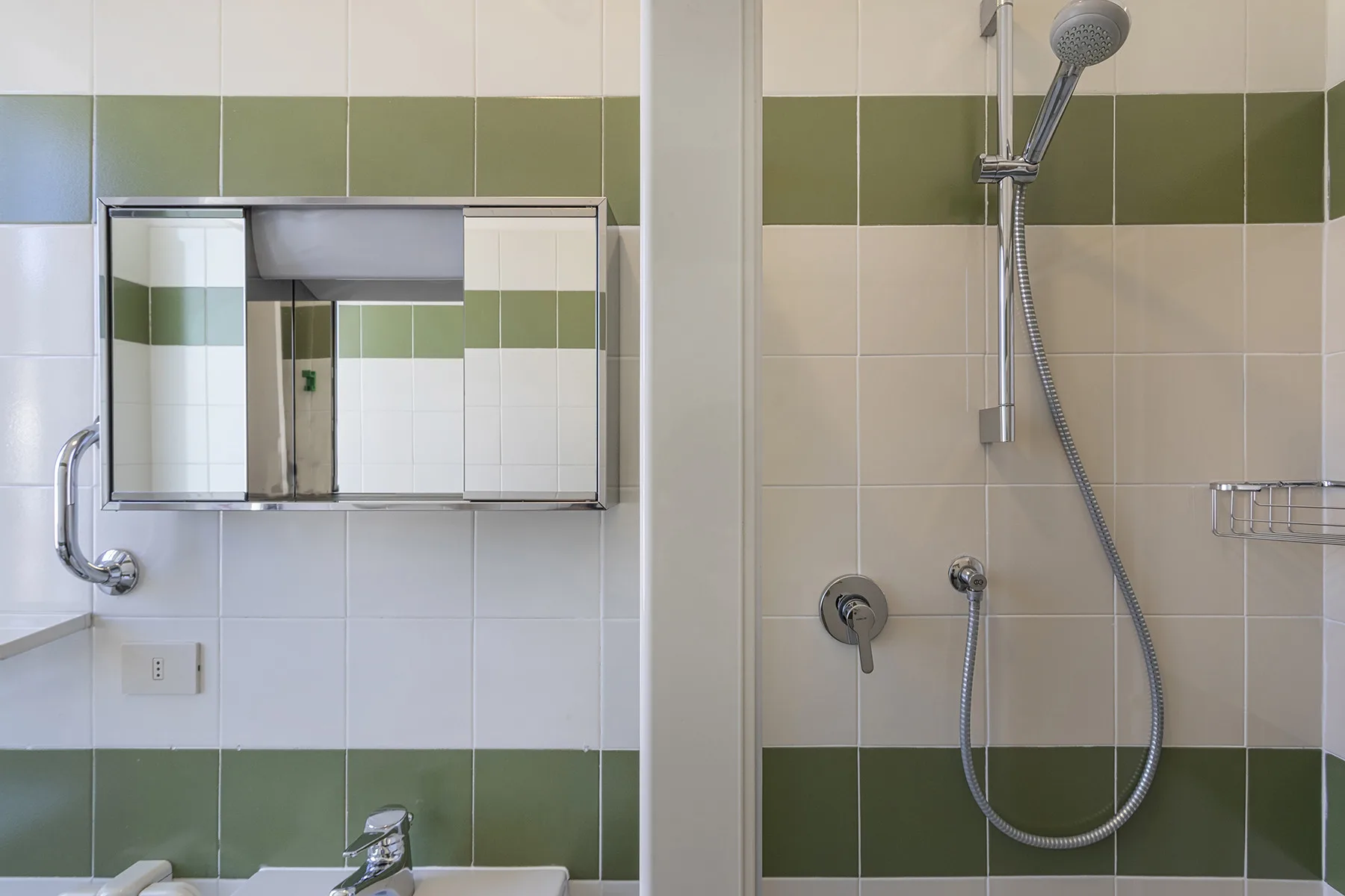 Un baño con azulejos, una ducha de pared y un armario con espejo.