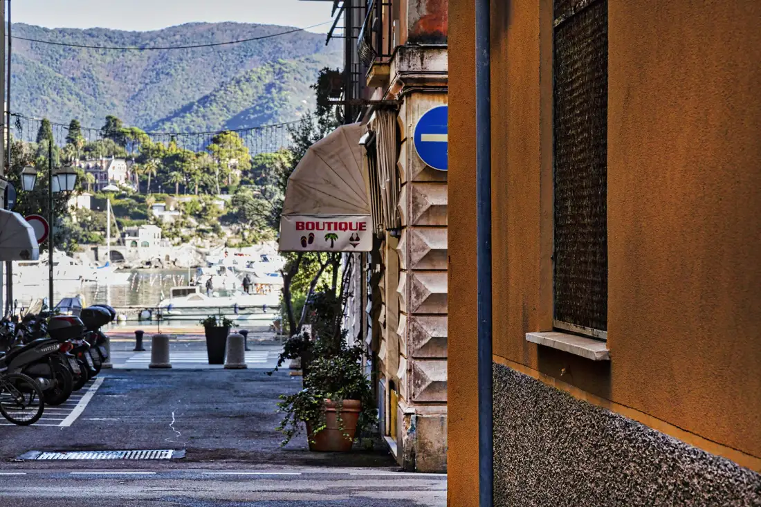 Una calle estrecha junto a un edificio se abre hacia la costa y colinas verdes.