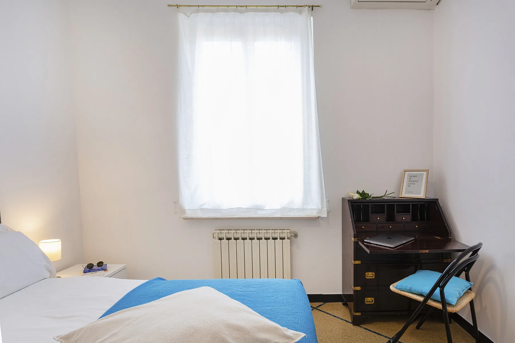Un dormitorio con una cama, un escritorio y una ventana luminosa.