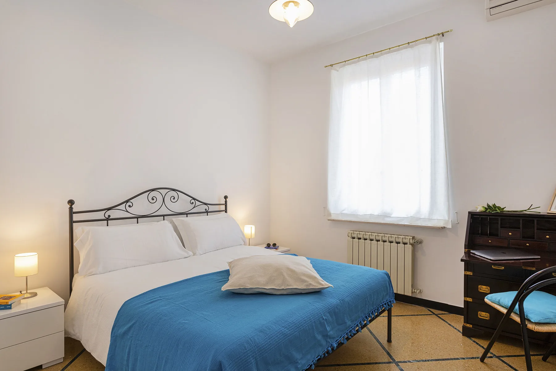 Un dormitorio con una cama cubierta de azul, una ventana luminosa y un escritorio.