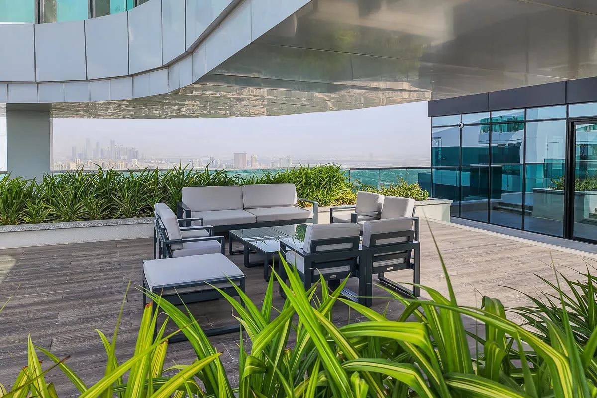 An outdoor terrace has a seating area beside glass walls and planted greenery.