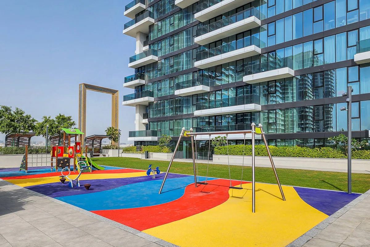 A colorful outdoor playground sits beside a modern glass building.