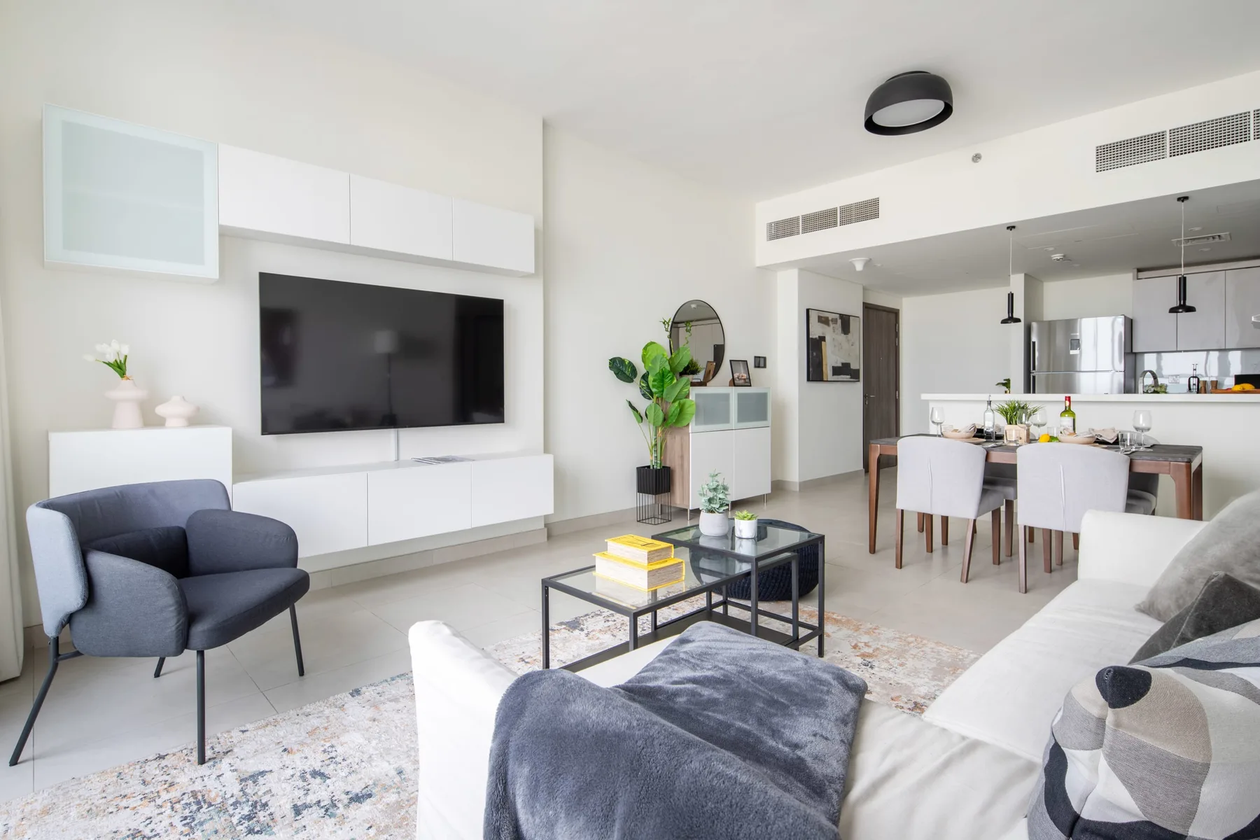 A bright living room opens onto a dining area, with a television above the built-in cabinets.