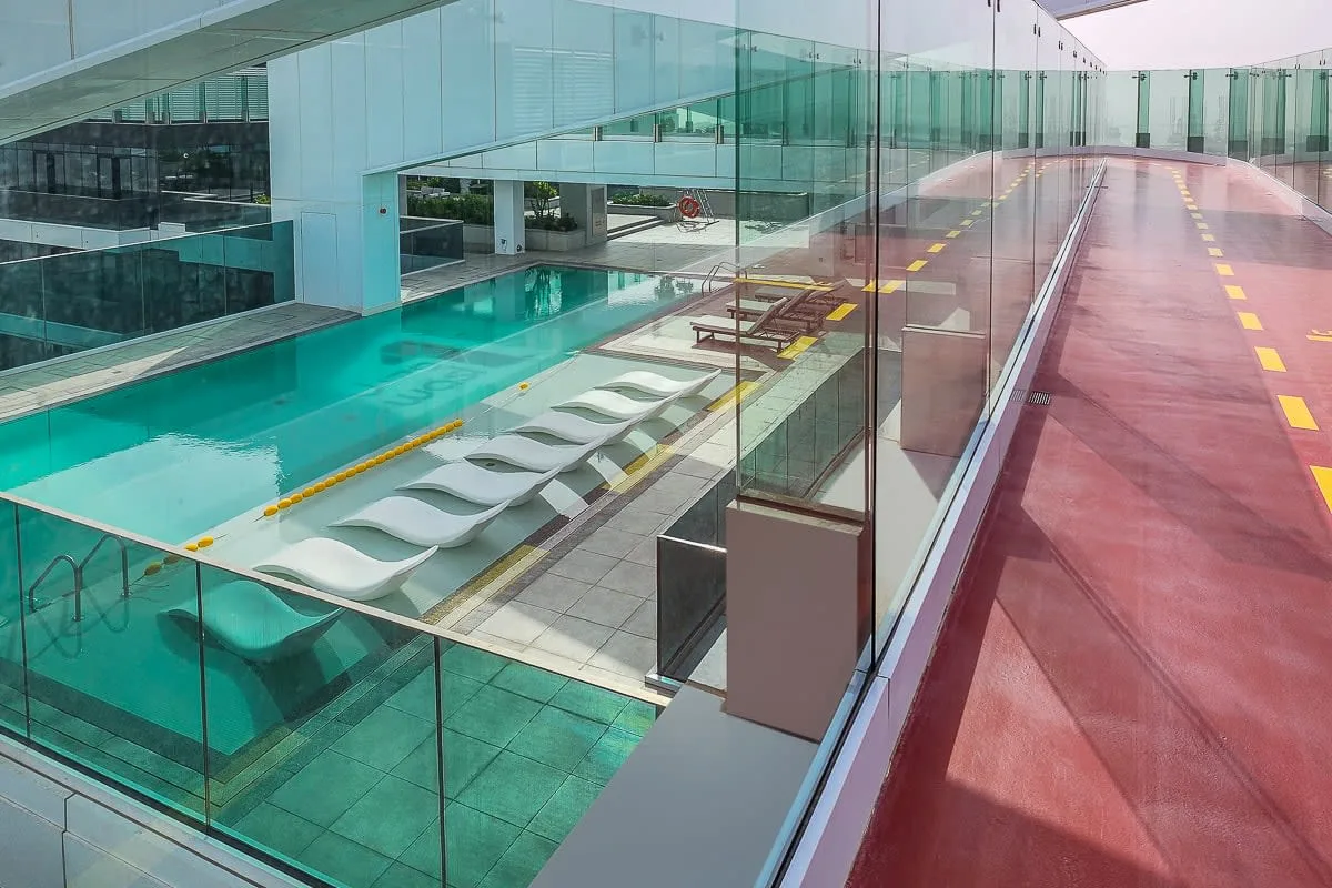 A modern swimming pool beside a glass walkway with lounge seating.