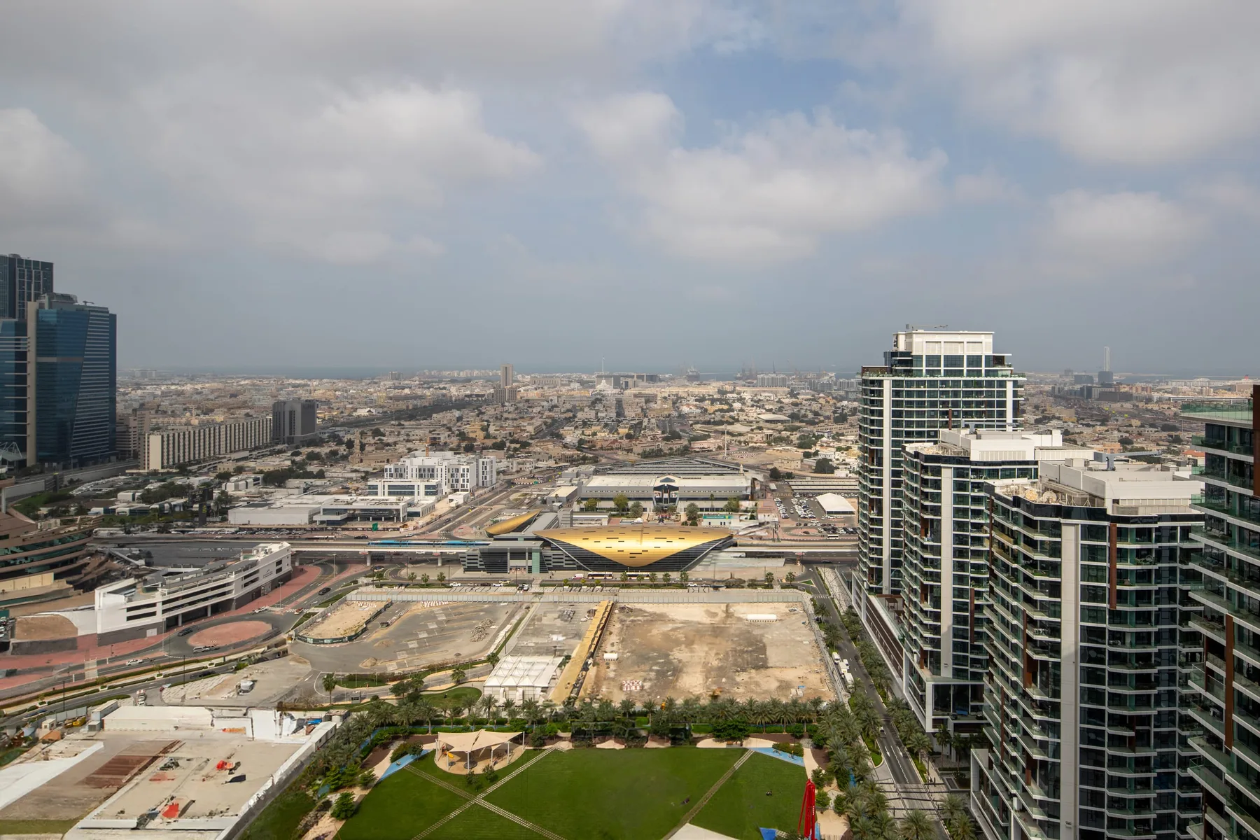 Cityscape with high-rise buildings, roads, and a landscaped green space in the foreground.