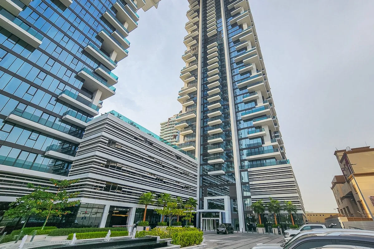 Modern high-rise buildings rise above a landscaped entrance plaza.