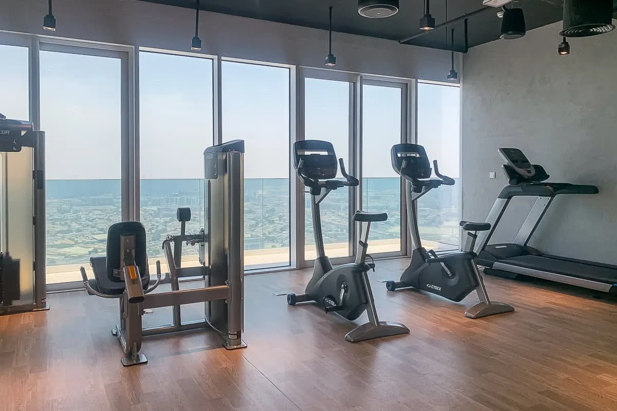 A fitness room with exercise bikes and treadmills beside large windows.