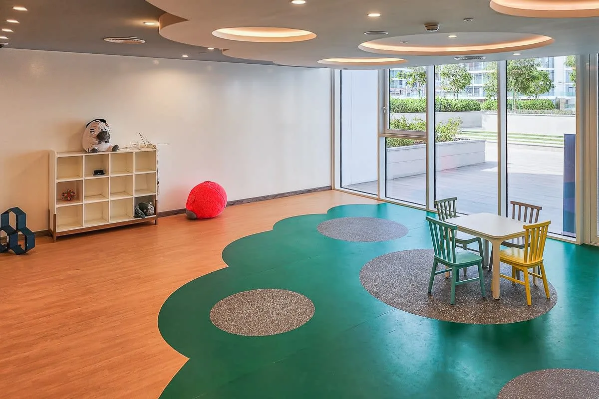 A bright activity room with a colorful floor and small table seating by the windows.