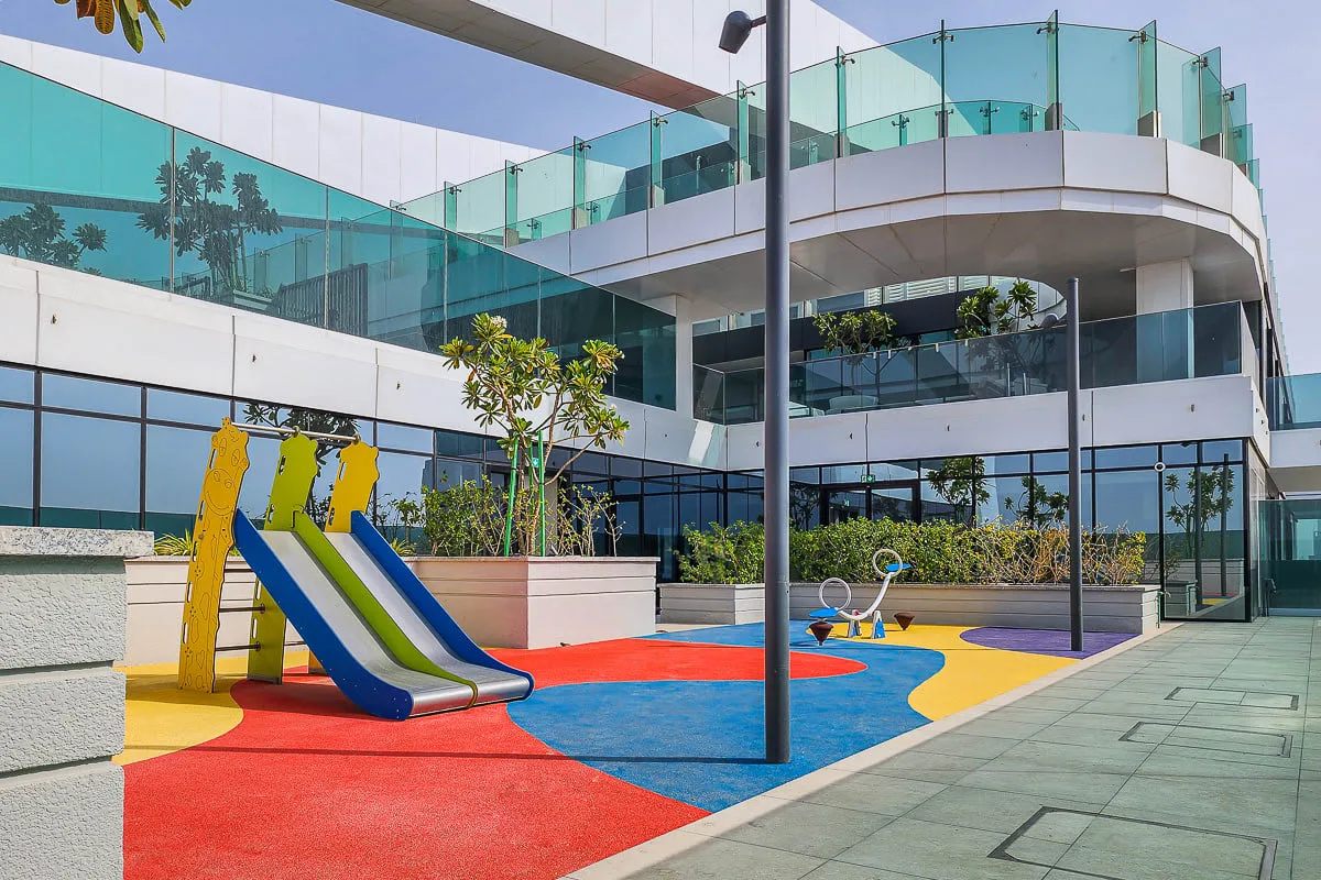 A colorful playground beside a modern building, with slides and a paved walkway.