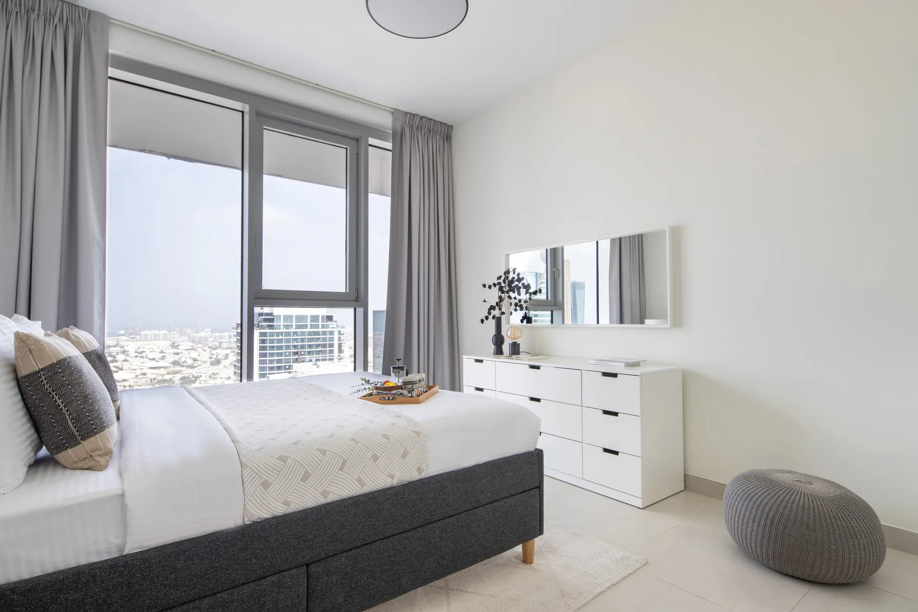 A bright bedroom with a bed, dresser, and large windows.