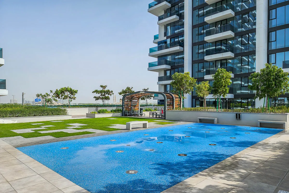 A blue swimming pool sits beside a modern glass-fronted building and landscaped grounds.