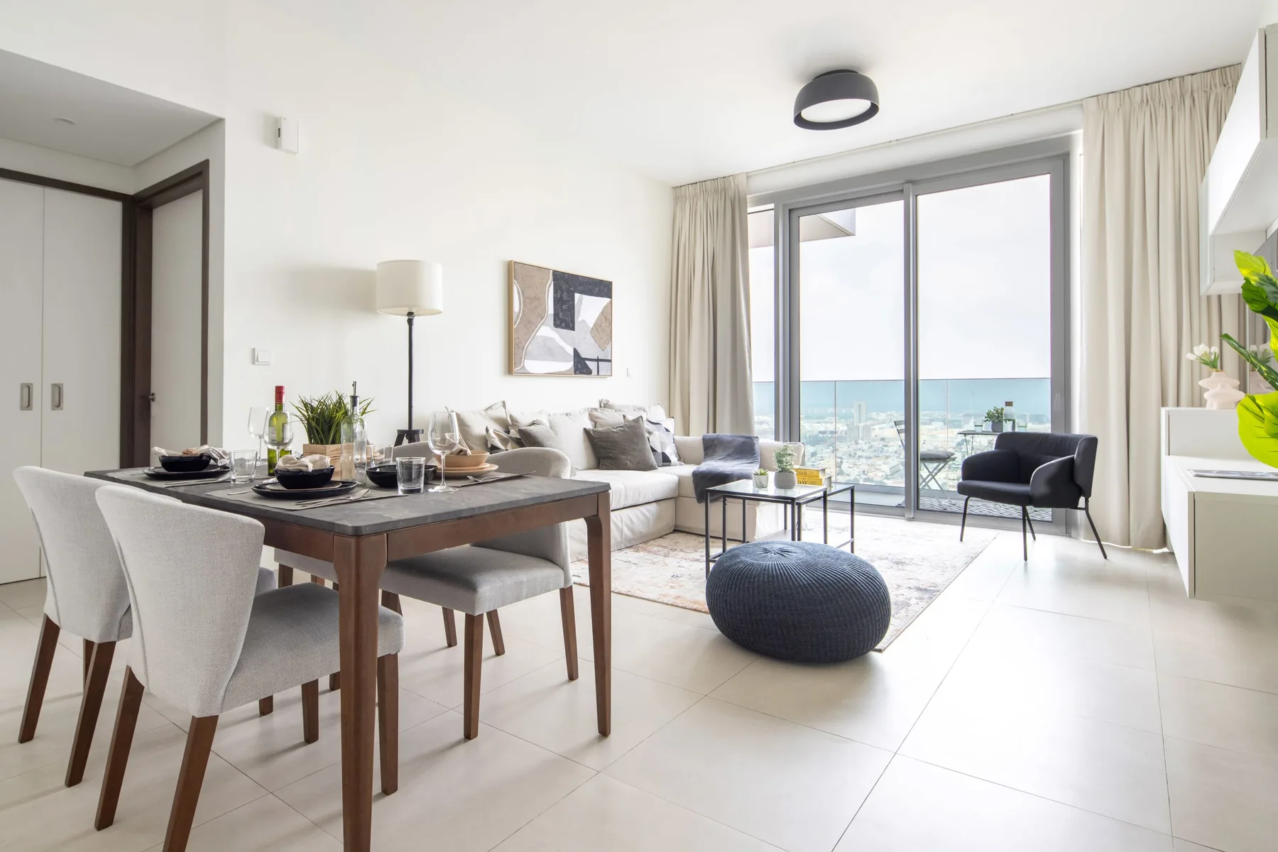 A bright living and dining area opens onto a balcony with a city view.