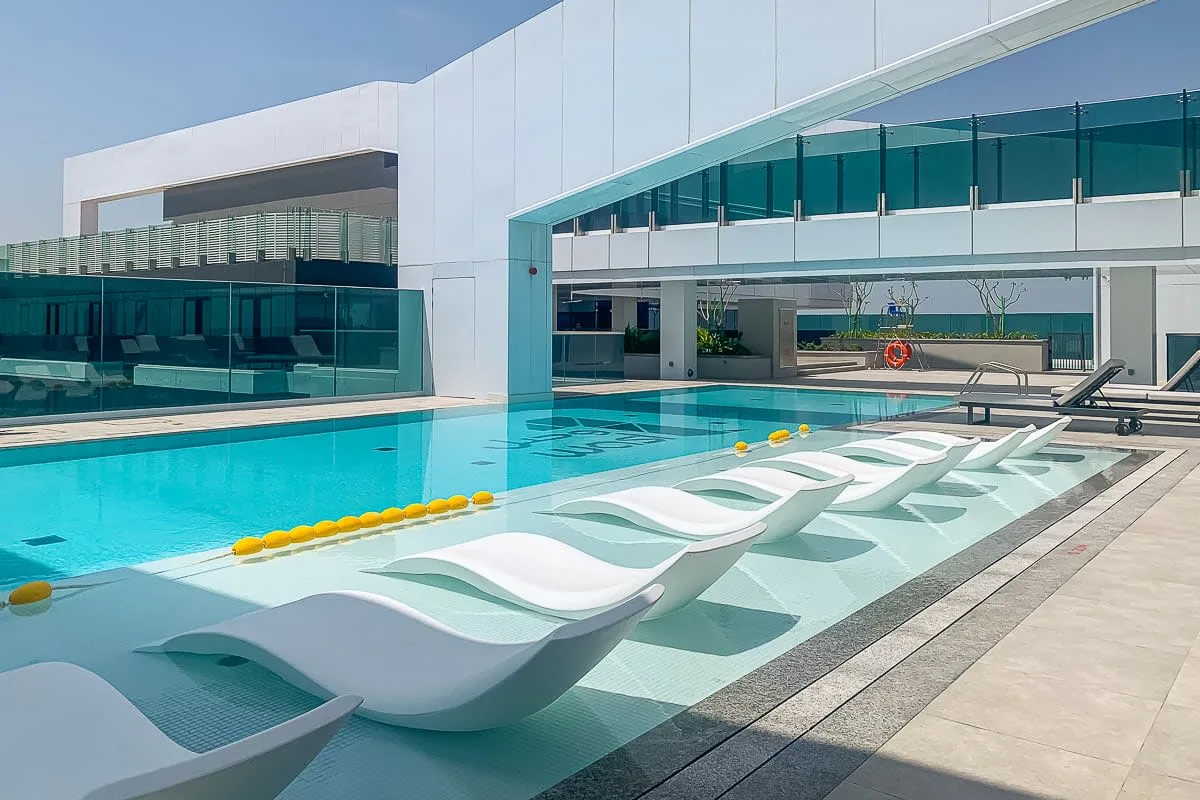 An outdoor swimming pool with white in-water loungers beside a modern building.