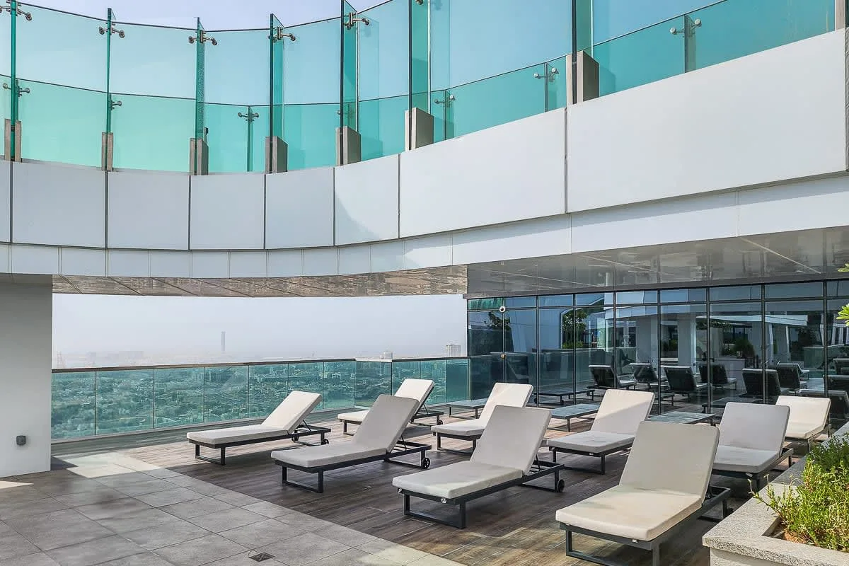 An outdoor poolside terrace with lounge seating and glass railings.