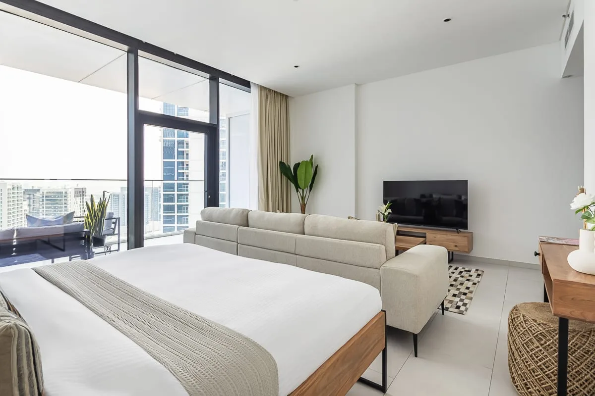 Un dormitorio luminoso con zona de estar, una cama grande y ventanales.