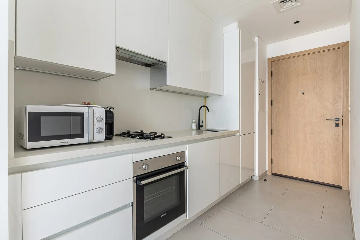 Una cocina compacta con gabinetes blancos, electrodomésticos sobre la encimera y una puerta de entrada de madera.