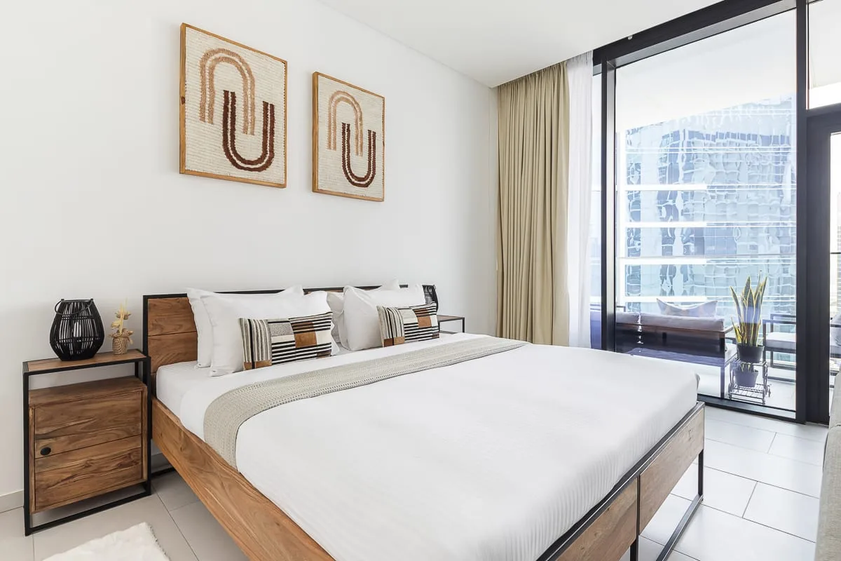 Un dormitorio luminoso con una cama grande junto a ventanales de suelo a techo.