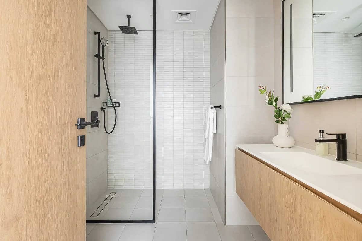 Un baño moderno con ducha de vidrio y un mueble de lavabo en tono madera.