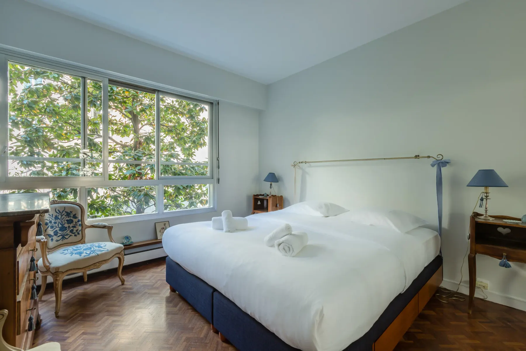 Un dormitorio con una cama grande junto a amplias ventanas con vistas a árboles frondosos.