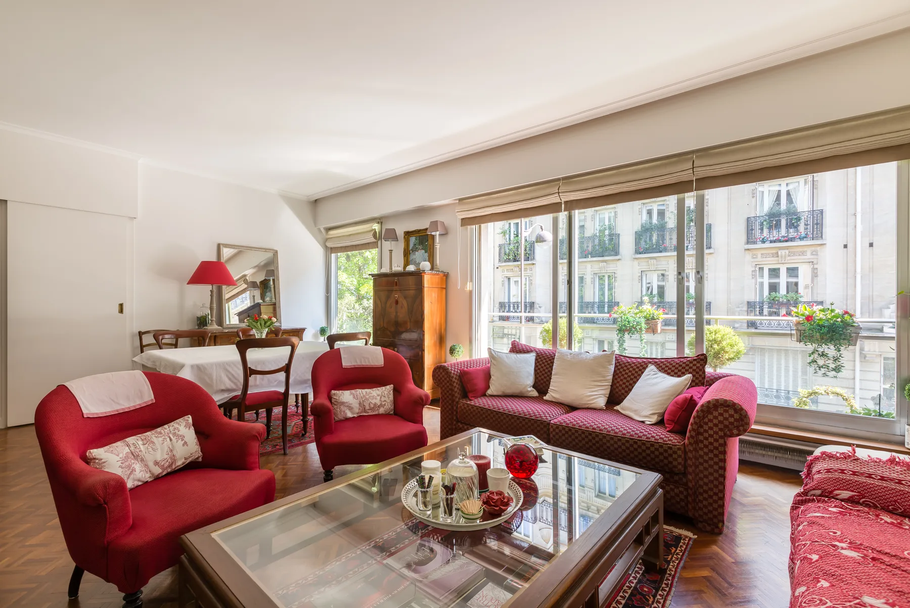 A bright living room with red seating, a glass coffee table, and large windows.