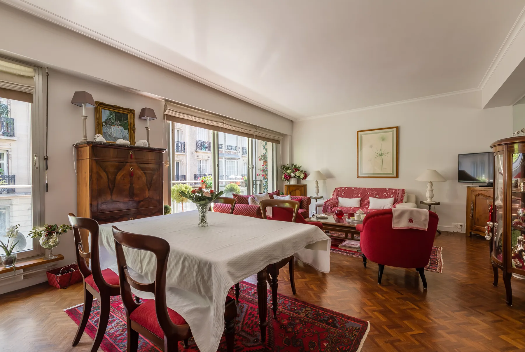 A dining and sitting room with a table, red seating, and large windows.