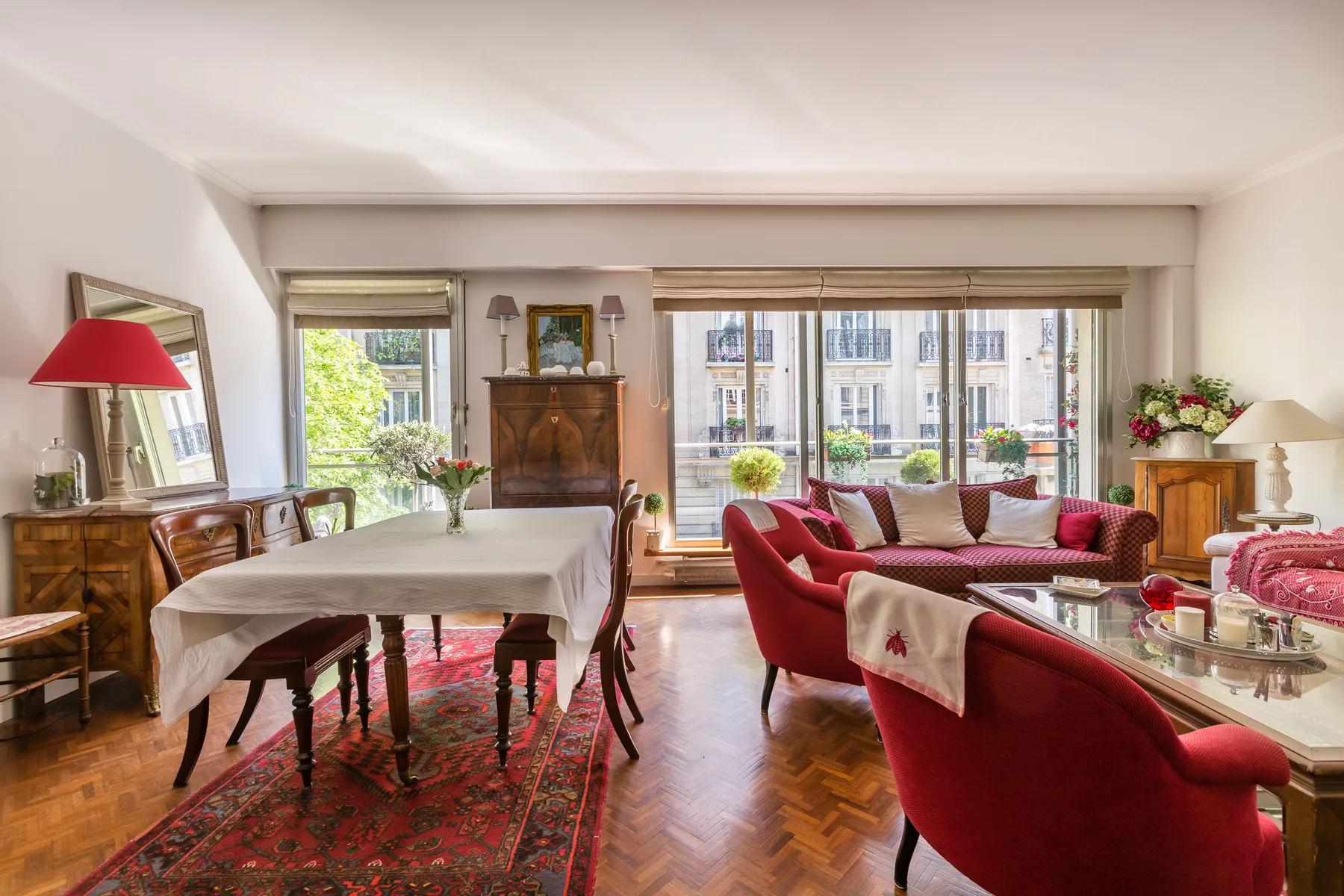 Una sala amueblada combina una mesa de comedor con asientos rojos junto a grandes ventanas.