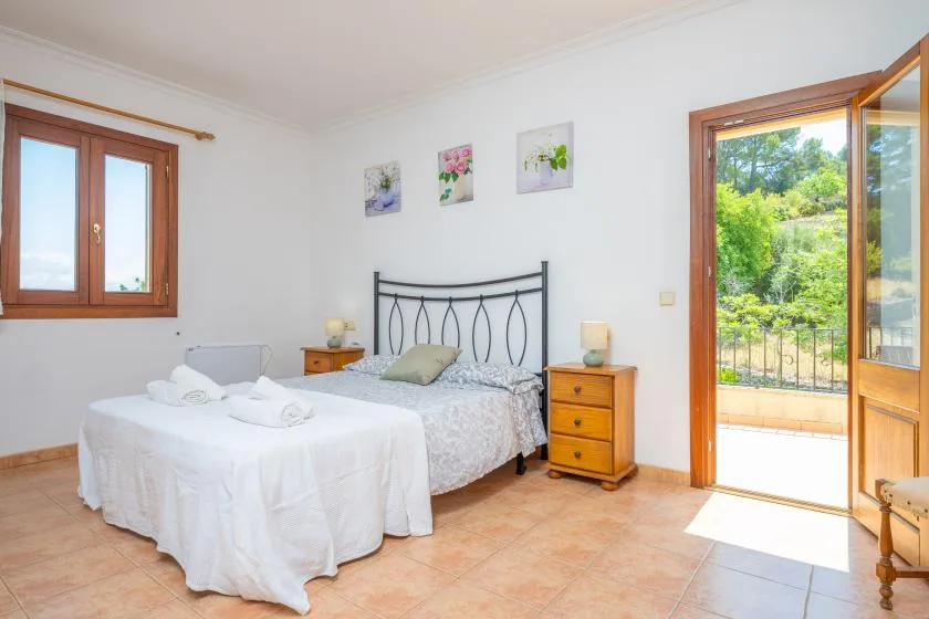 Un dormitorio luminoso con dos camas, mesitas de noche y una puerta abierta hacia la vegetación.