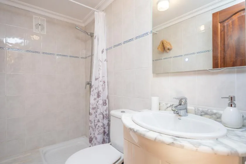 Un baño con lavabo, espejo y ducha detrás de una cortina.