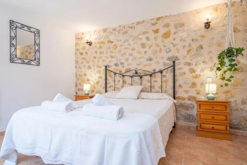 Un dormitorio con una cama bien tendida, mesitas de noche y una pared de piedra.
