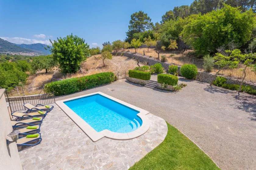 Una piscina al aire libre está junto a un patio pavimentado y una ladera ajardinada.