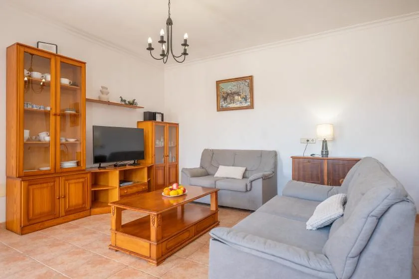 Una sala de estar con asientos grises, muebles de madera y un televisor.