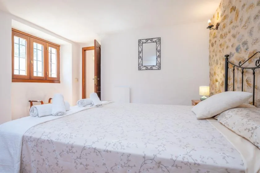 Un dormitorio con una cama bien hecha, una ventana con marco de madera y una pared de piedra.