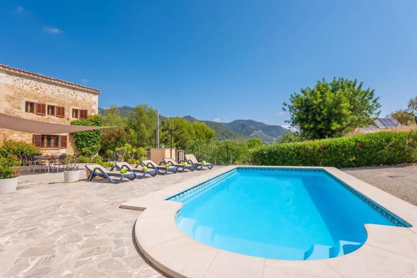 Una piscina está en un patio de piedra junto a una casa y un jardín.