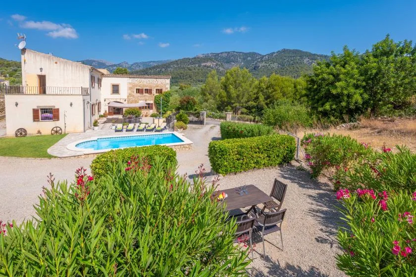 Zona ajardinada con piscina junto a una casa, asientos de jardín y colinas al fondo.