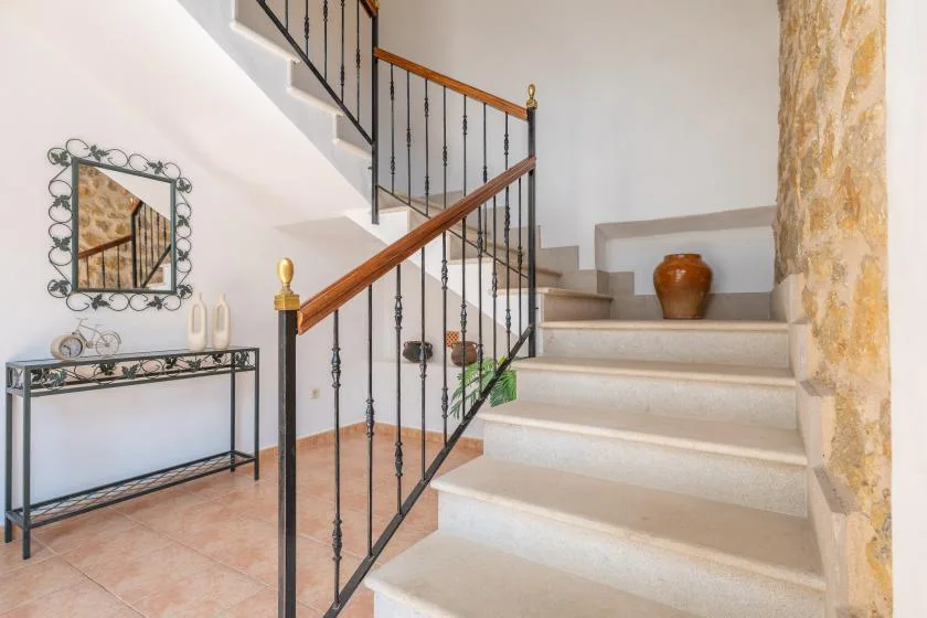 Una escalera interior con barandillas oscuras sube junto a una pared de piedra.