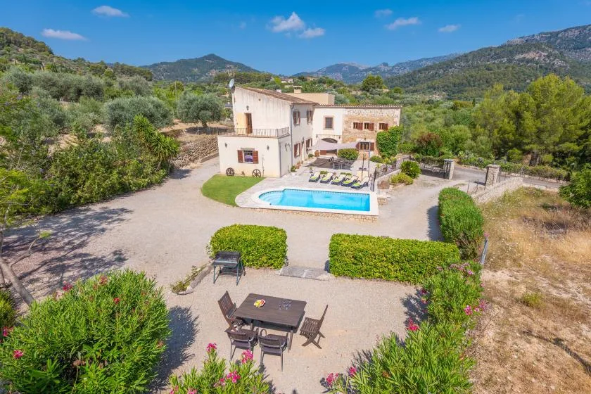 Una casa en una ladera con piscina, patio y colinas verdes alrededor.