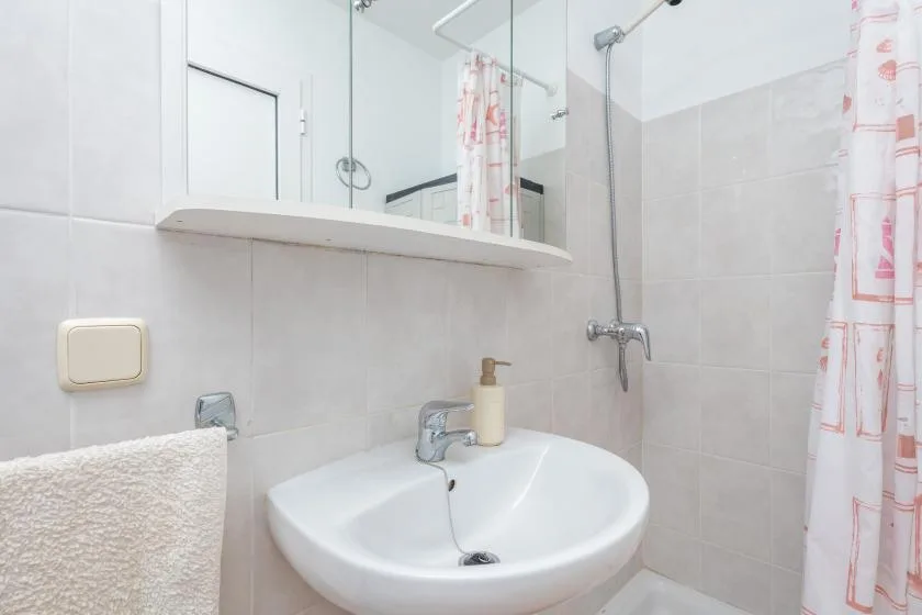 Un baño alicatado con lavabo, espejo y cortina de ducha estampada.