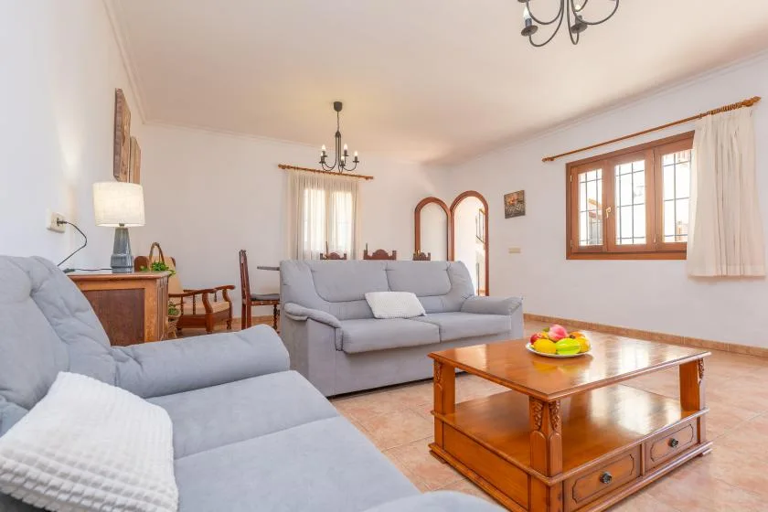 Una sala de estar con asientos grises, una mesa de centro de madera y ventanas.