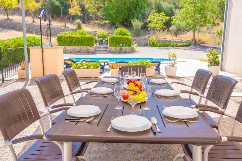 Una mesa de comedor al aire libre está puesta con platos junto a una piscina.