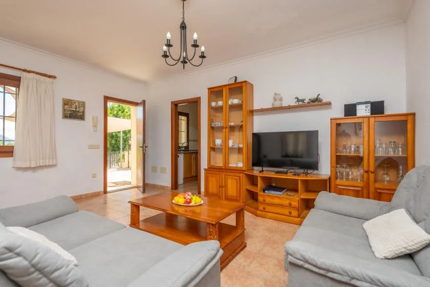 Una sala luminosa con asientos grises, una mesa de centro de madera y un televisor.