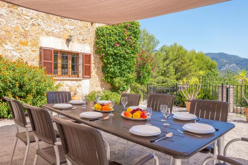 Comedor al aire libre con la mesa puesta junto a un muro de piedra y un jardín.