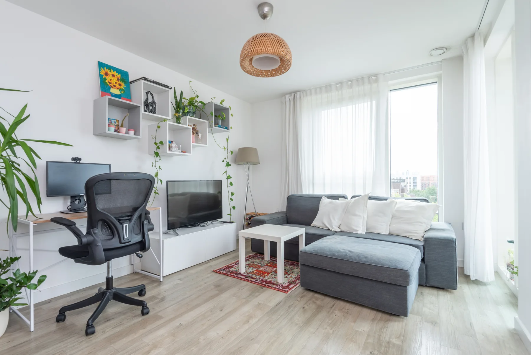 Una sala luminosa con un sofá seccional gris y ventanas grandes.