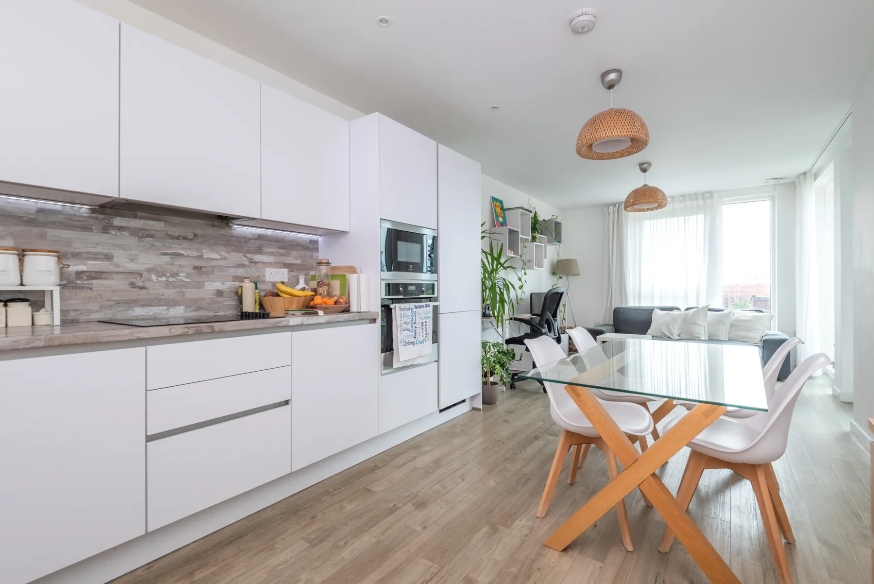 Cocina y comedor diáfanos y luminosos, con una mesa de vidrio y armarios blancos.