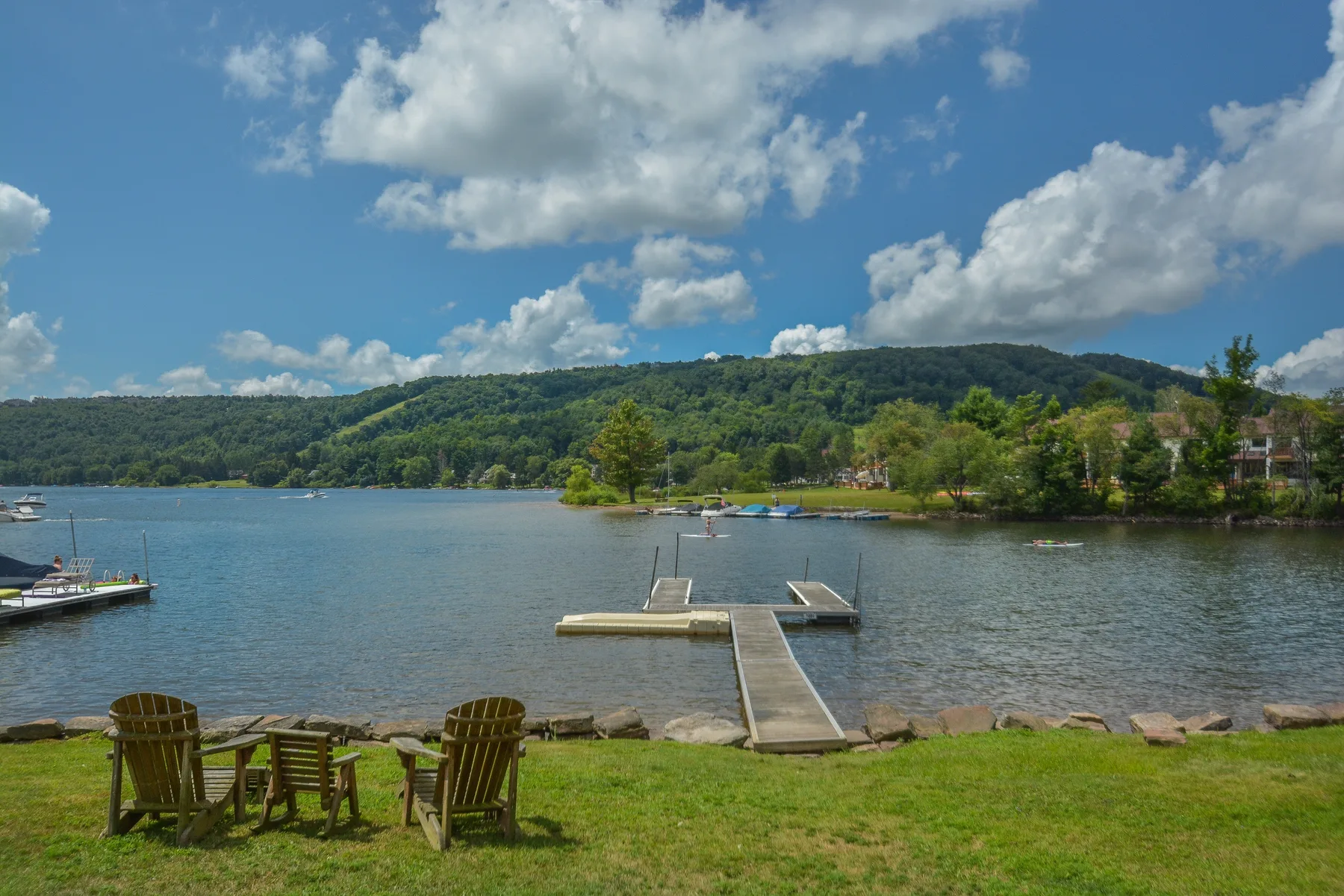 A lakeside scene with a dock extending into the water and chairs on the grassy shore.